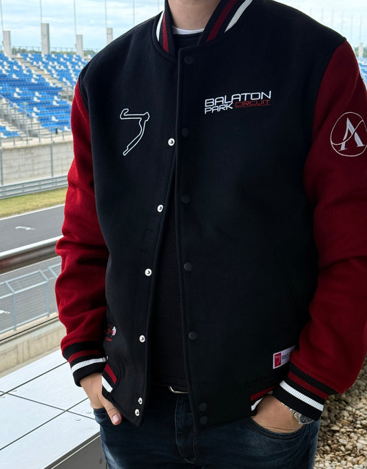 Person wearing a black and red varsity jacket with logos, standing outdoors.